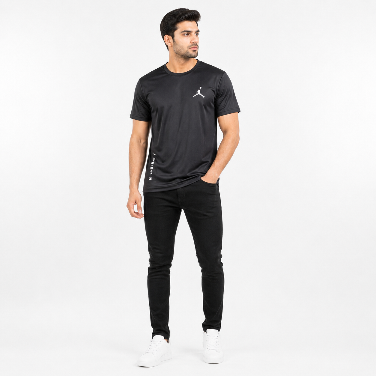 A man modeling a black short-sleeve athletic t-shirt with a white Jumpman logo on the chest, paired with black pants and white sneakers, against a plain white studio background.