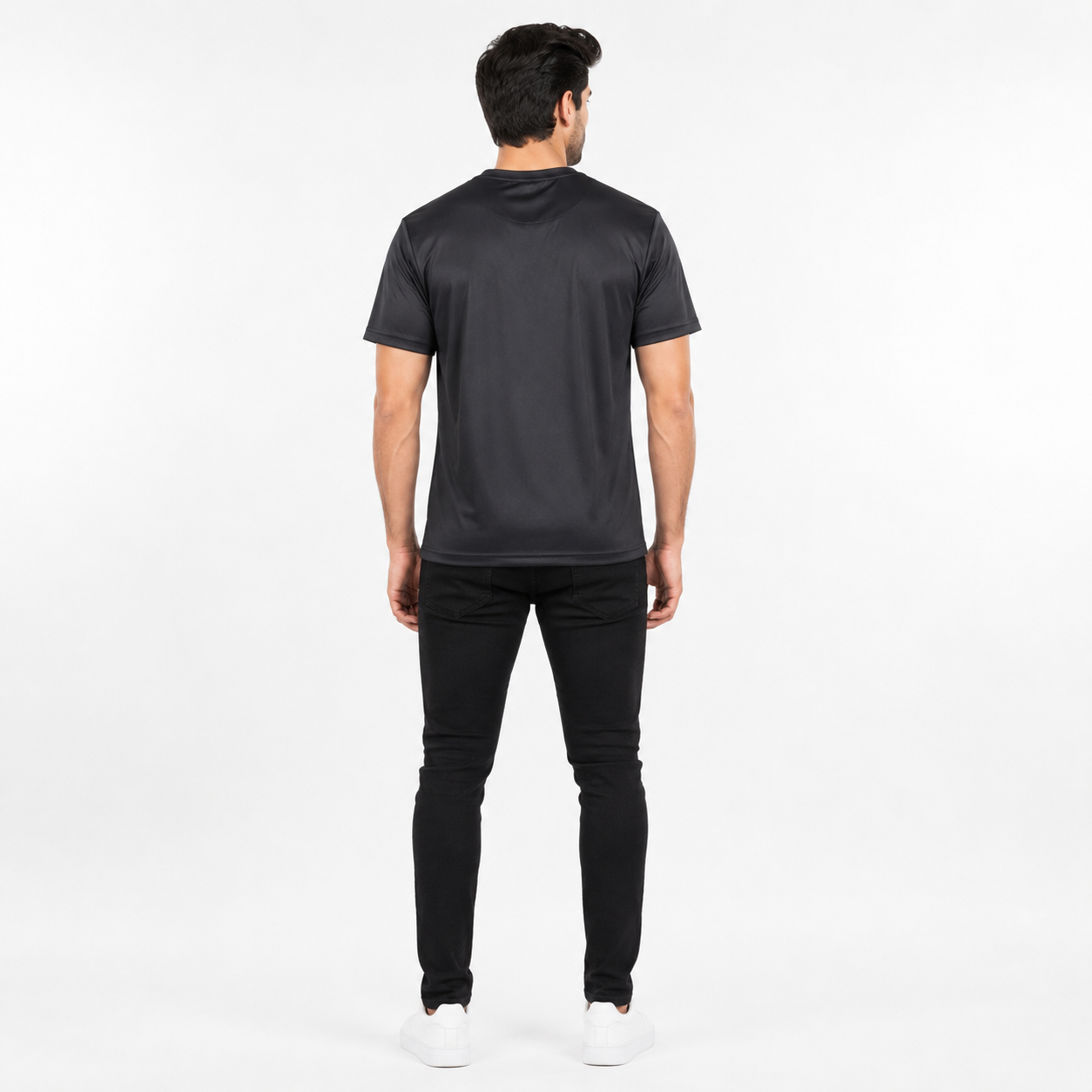 A man viewed from behind wearing a black short-sleeve t-shirt, black pants, and white sneakers against a plain white studio background.