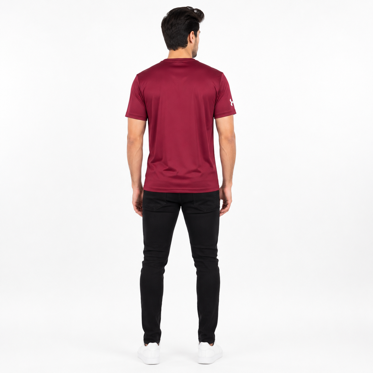 A man viewed from behind wearing a maroon short-sleeve athletic t-shirt, black pants, and white sneakers against a plain white studio background.