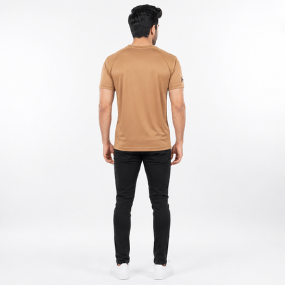 A man viewed from behind wearing a tan short-sleeve athletic t-shirt, black slim-fit pants, and white sneakers against a plain white studio background.