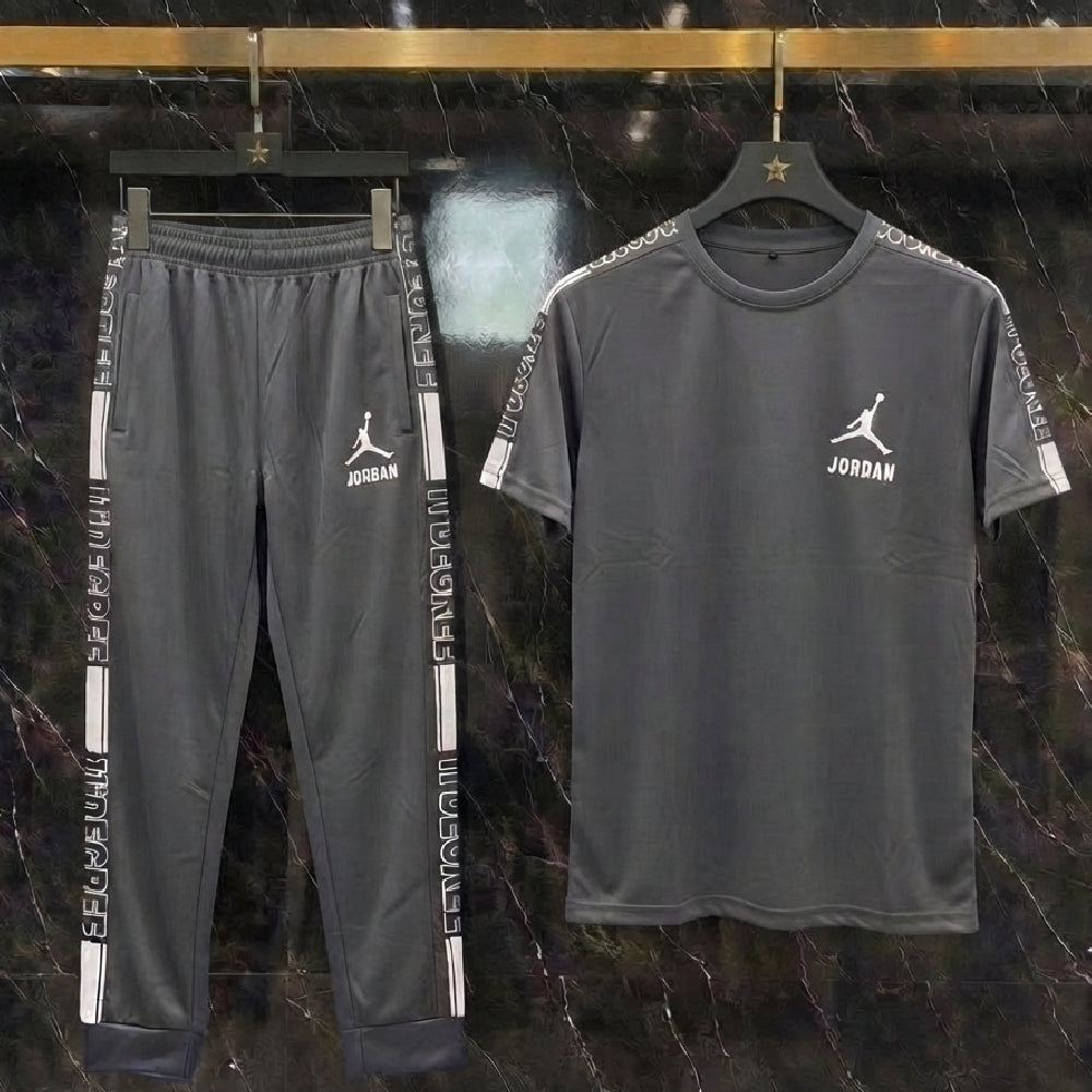 A dark gray two-piece athletic set featuring a short-sleeve t-shirt and matching sweatpants, both hanging on black hangers against a dark marble wall. The t-shirt and pants have white Jordan Jumpman logos and 'JORDAN' text on the chest and sleeve cuffs.
