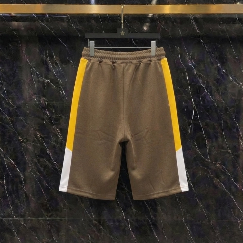 A pair of brown athletic shorts with yellow and white side stripes, hanging on a black hanger against a dark marble background.