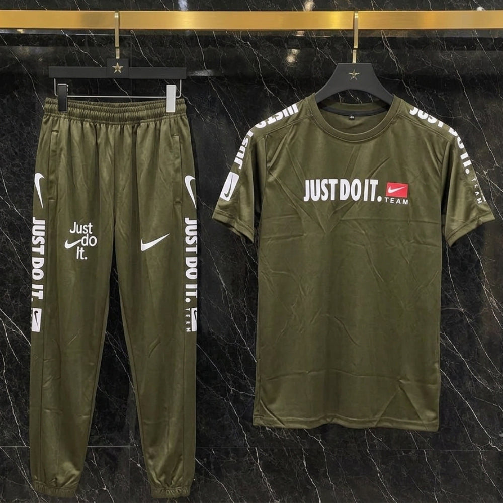 An olive green Nike tracksuit set consisting of a short-sleeve t-shirt and matching jogger pants, displayed on hangers against a black marble background. The t-shirt features 'JUST DO IT.