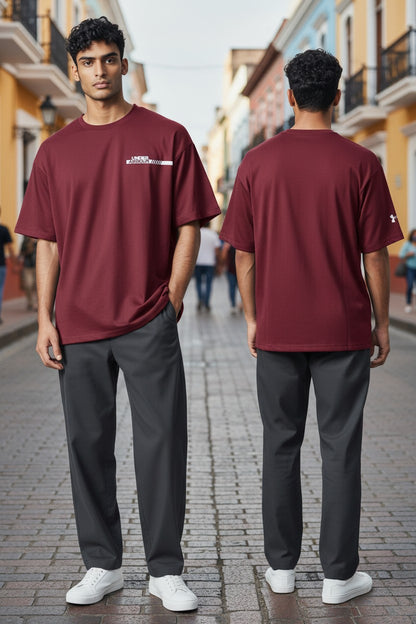 A man modeling a burgundy short-sleeve t-shirt and dark gray trousers, shown from both the front and back views on a cobblestone street.