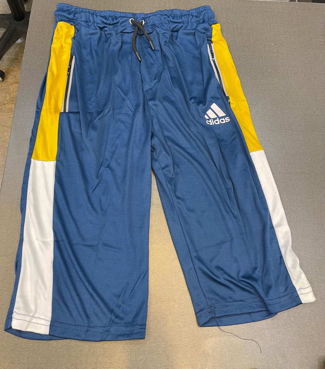 Blue Adidas athletic shorts with yellow and white side panels, laid flat on a gray surface.