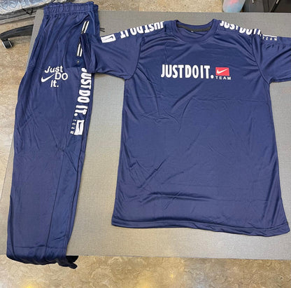 A navy blue Nike athletic tracksuit set consisting of a short-sleeve t-shirt and matching sweatpants, laid flat on a gray surface. The t-shirt features 'JUSTDOIT.
