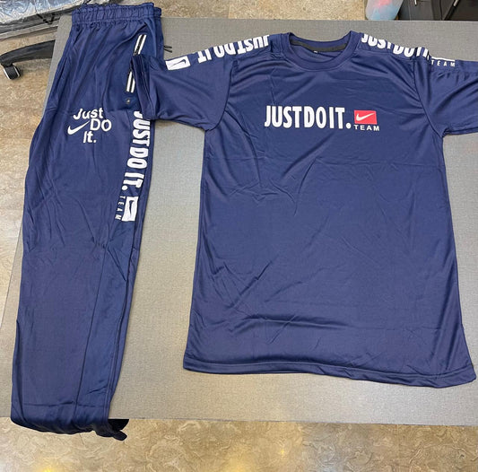 A navy blue Nike athletic tracksuit set consisting of a short-sleeve t-shirt and matching sweatpants, laid flat on a gray surface. The t-shirt features 'JUSTDOIT.