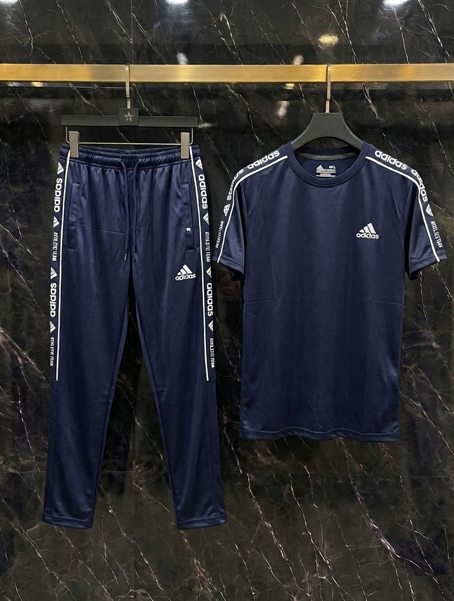 A navy blue Adidas tracksuit set consisting of a short-sleeve t-shirt and matching jogger pants, hanging on black hangers against a dark marble-patterned wall.